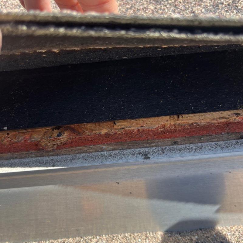 Roof decking showing water damage beneath lifted shingles