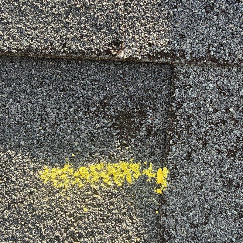 Asphalt roof shingle with hail damage marked in yellow