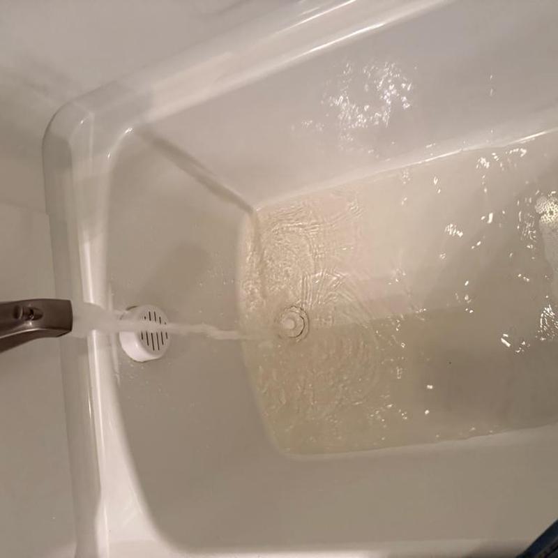 Bathtub faucet running with water flowing into tub