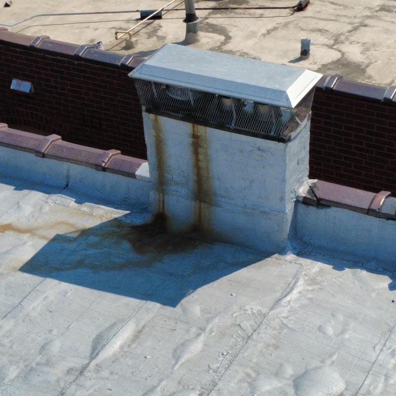 Flat roof with rust-stained chimney and roofing membrane