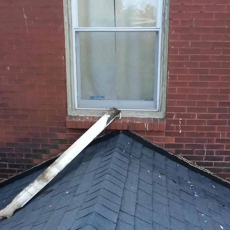 Window outlet drain pipe on shingled roof below brick wall