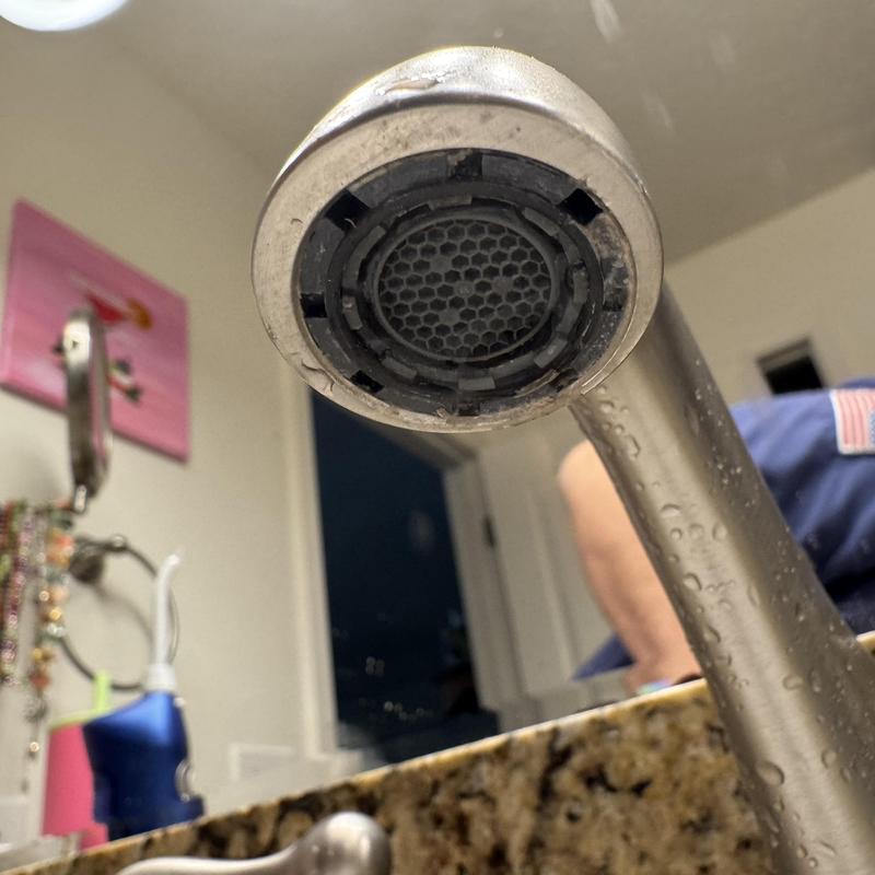 Bathroom faucet aerator clogged with debris and water droplets Bathroom faucet aerator clogged with debris and water droplets