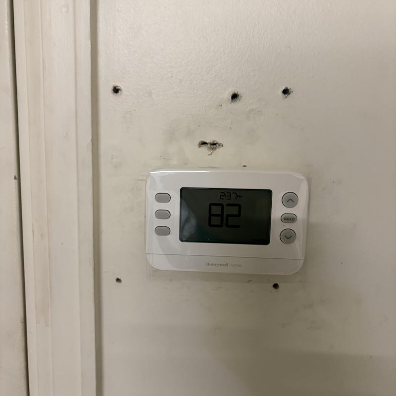 Heat pump thermostat mounted on wall with damage holes Heat pump thermostat mounted on wall with damage holes