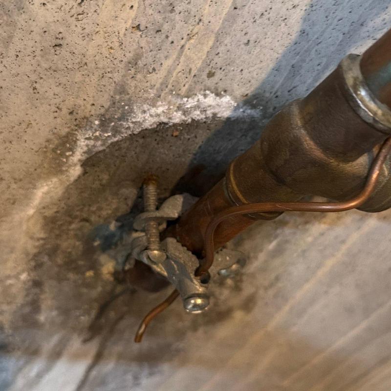 Copper plumbing pipe with secured grounding clamp on concrete wall
