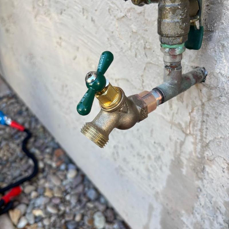 Outdoor hose bib valve with green handle on exterior wall