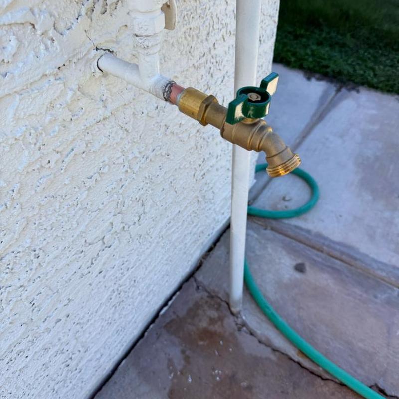 Brass hose bibb with green handle on exterior wall