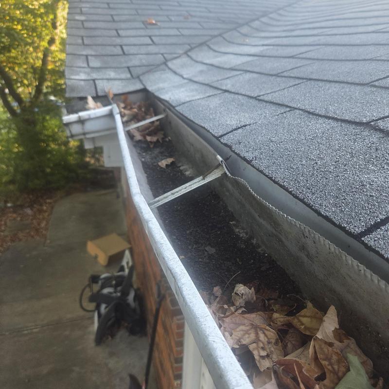 Gutter filled with leaves and debris on shingle roof edge