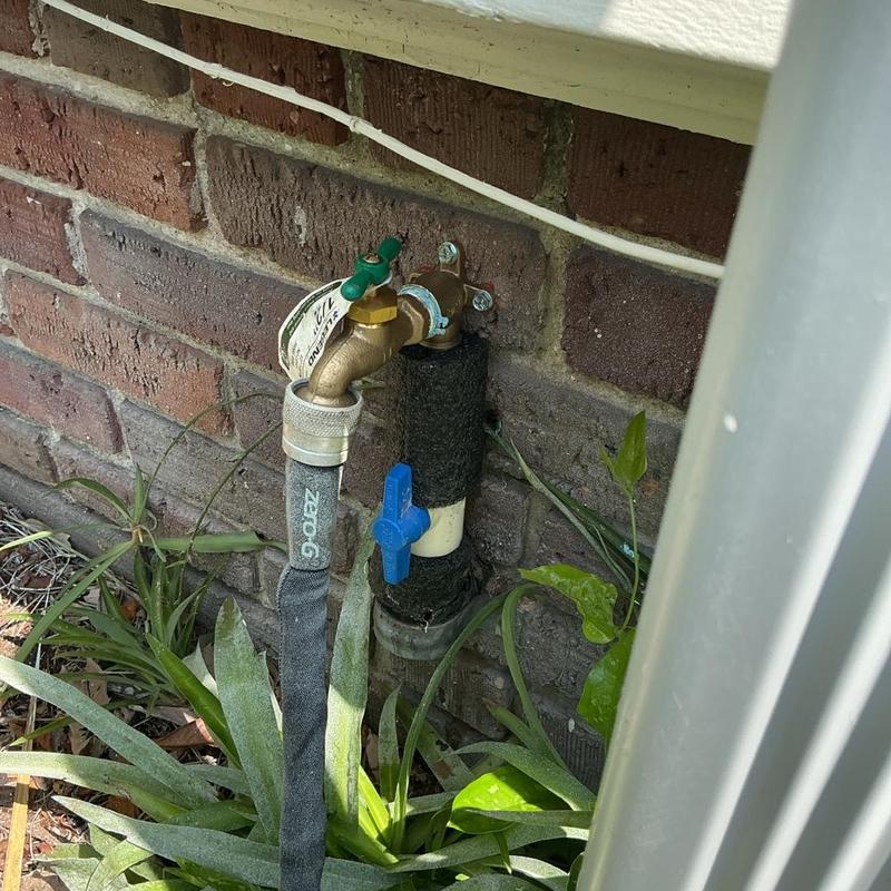 Exterior hose bib with attached garden hose near brick wall Exterior hose bib with attached garden hose near brick wall