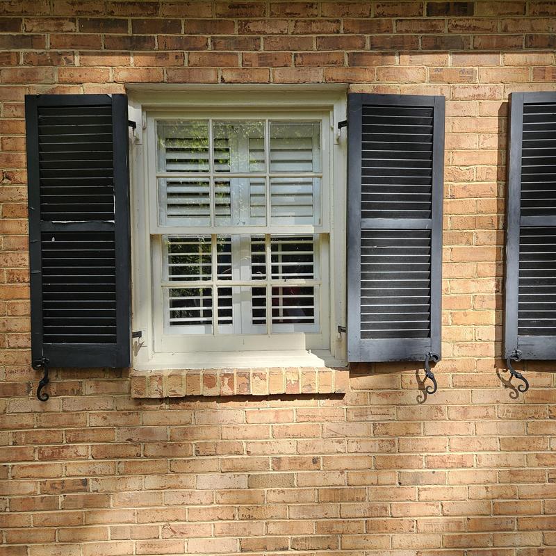 Double-hung window with black shutters on brick wall