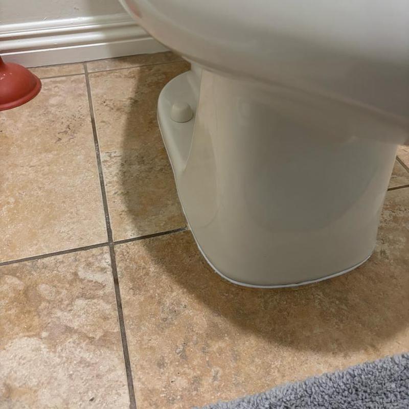 Toilet base sealed with clear adhesive caulk on tile floor