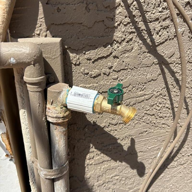 Hose bib with green valve and PVC piping on stucco wall