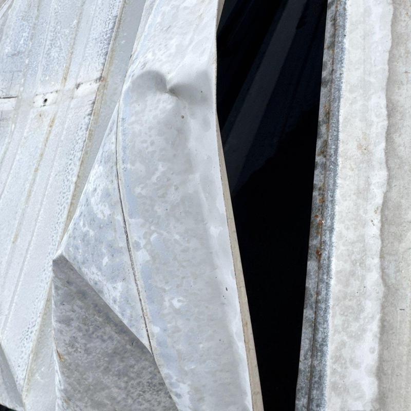 Metal roof panel with hail damage dent and tear