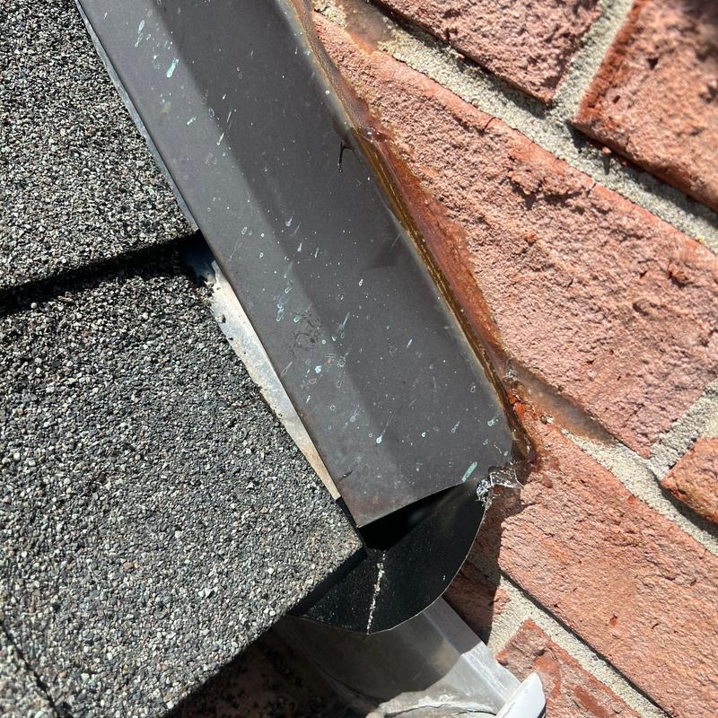 Roof flashing edge near brick wall with shingle roof