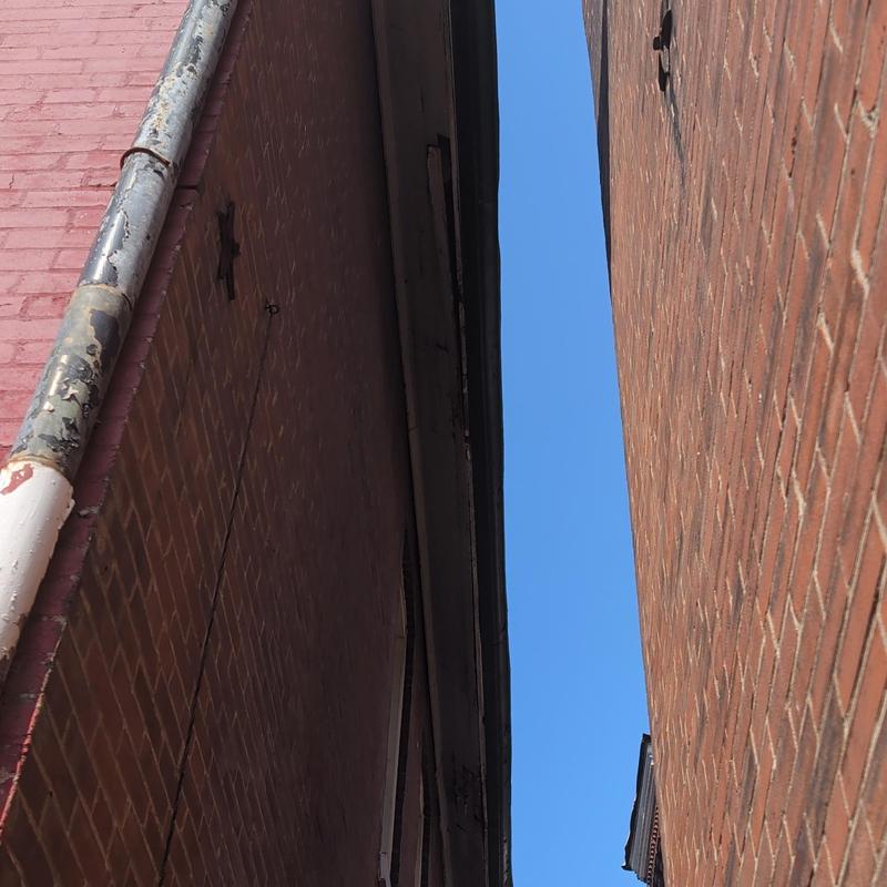 Damaged gutter and downspout between brick buildings
