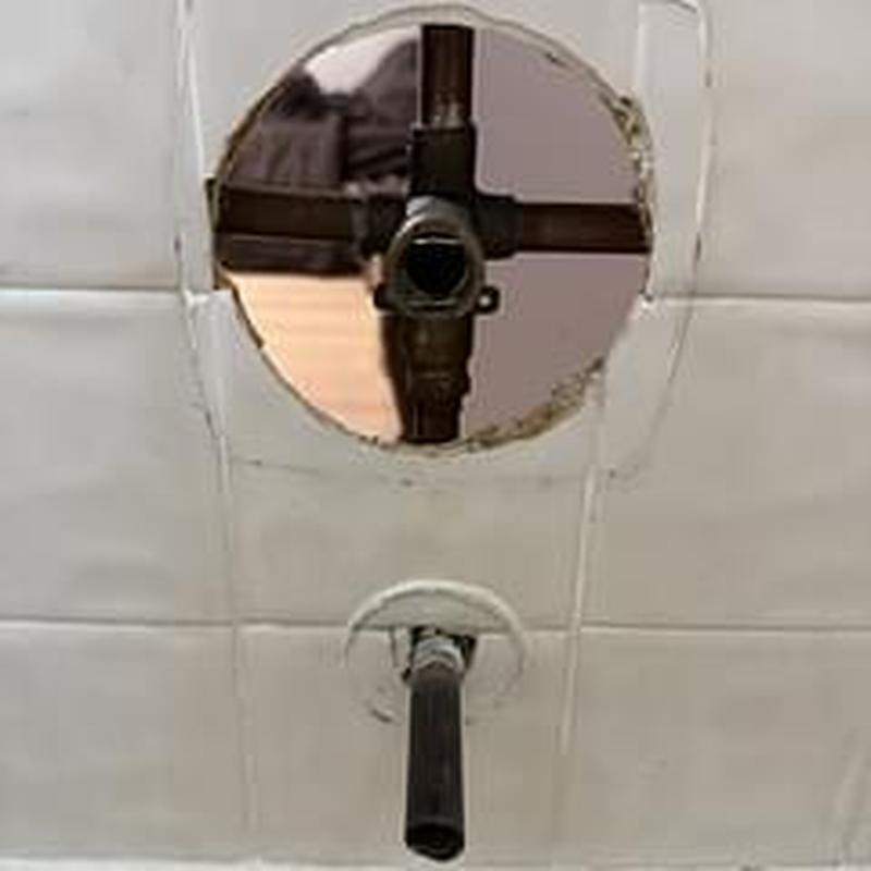 Shower valve plumbing exposed behind tile wall