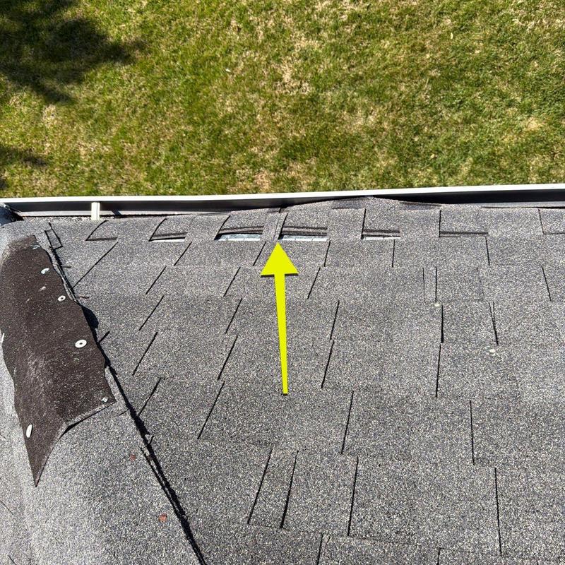 Roof shingles with lifted and missing sections near gutter