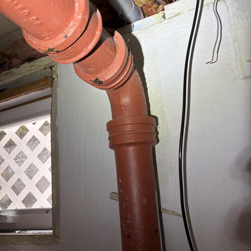 Cast-iron drain pipe with elbow joint in basement wall