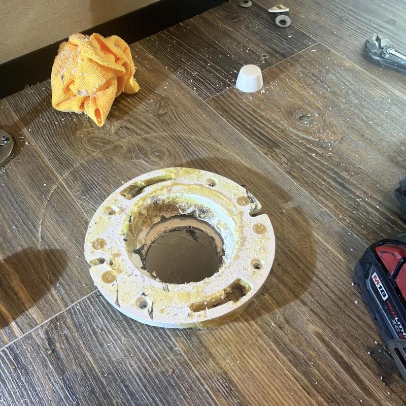 Toilet flange on wood floor with cut marks and debris