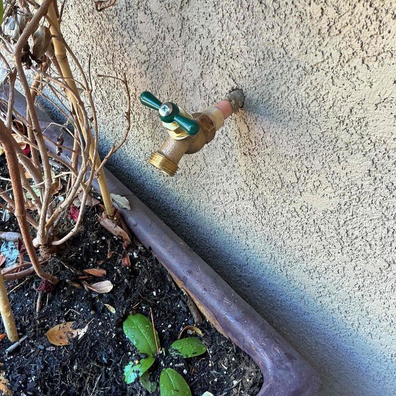 Outdoor hose bibb with green handle on stucco wall