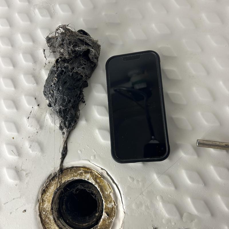 Shower drain with hair clog removed next to phone Shower drain with hair clog removed next to phone