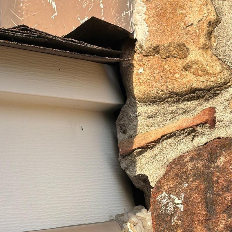 Vinyl siding corner damage near stone wall and window