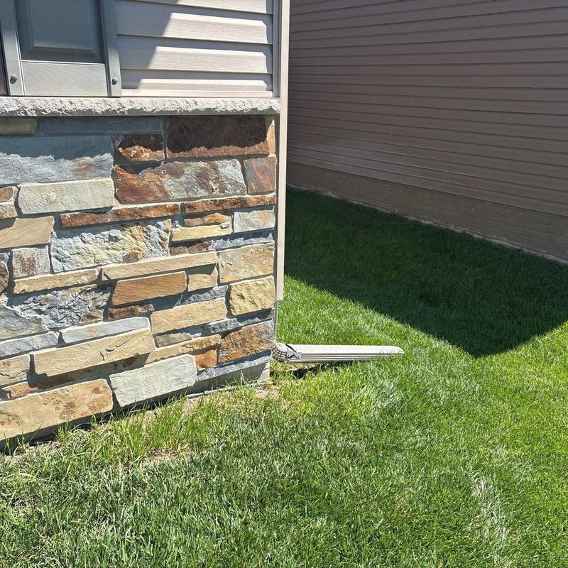 Gutter downspout extension next to stone house wall Gutter downspout extension next to stone house wall