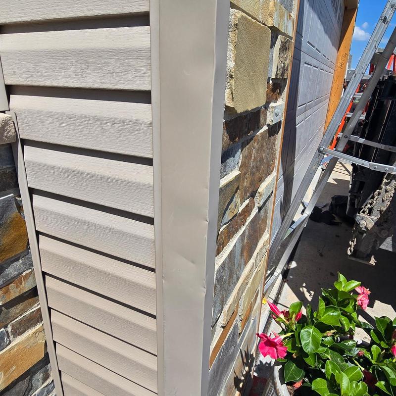 Vinyl siding corner trim beside stone facade in sunlight Vinyl siding corner trim beside stone facade in sunlight