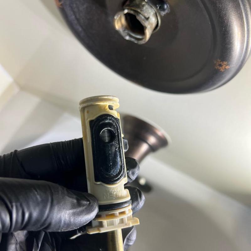 Moen shower cartridge held by gloved hand near valve housing