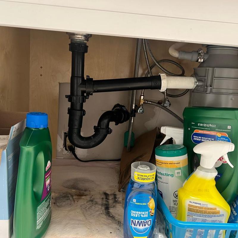 Kitchen sink drain pipes with cleaning supplies nearby
