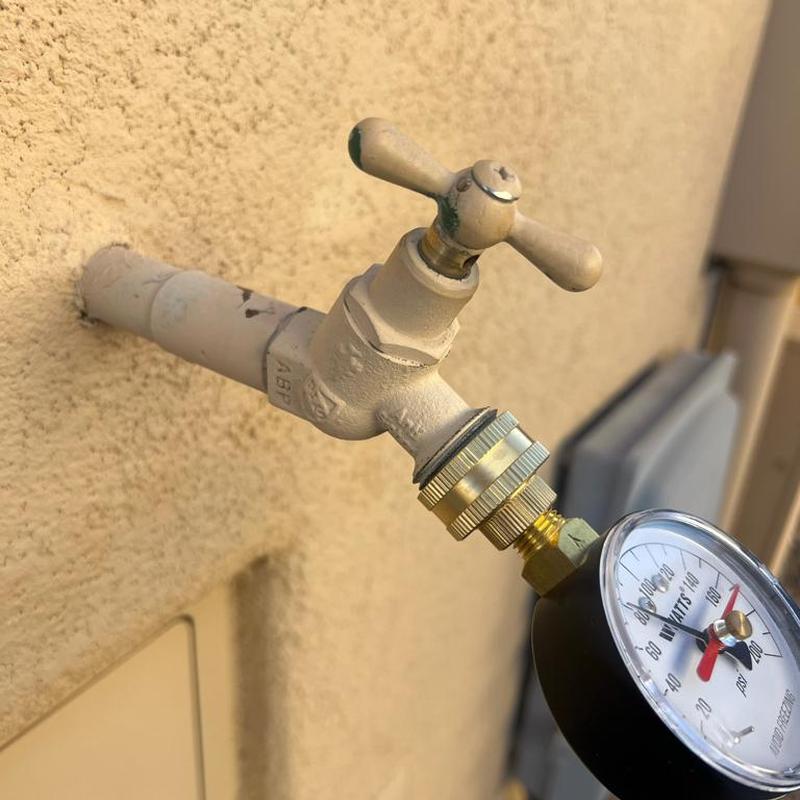 Hose bib with attached water pressure gauge on exterior wall