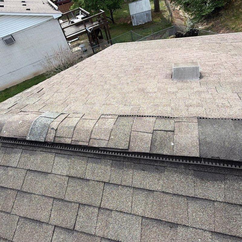 Asphalt shingles with visible wear and damage on ridge line