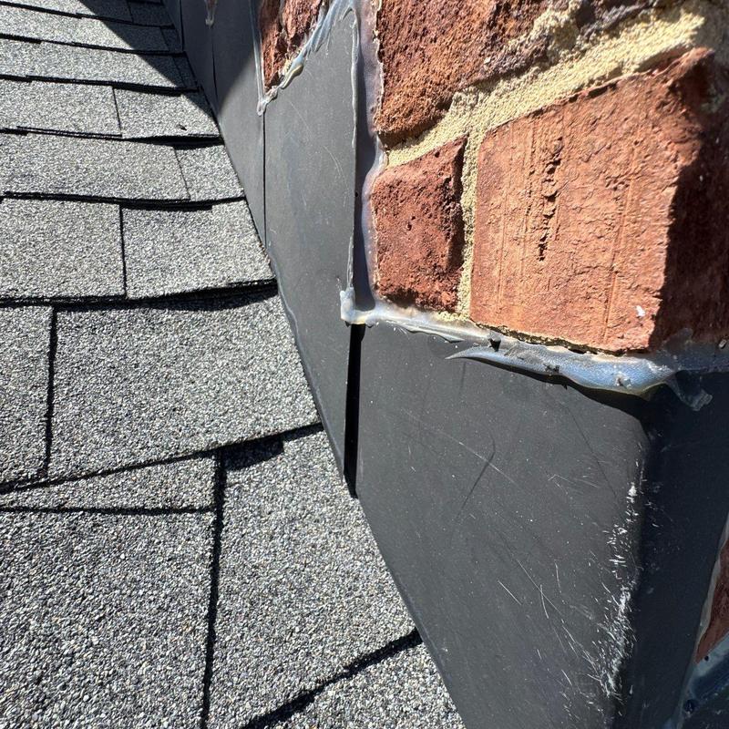Roof flashing and shingle edges near brick wall inspection