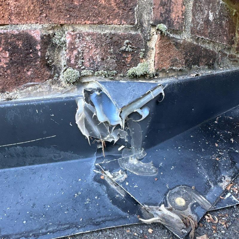 Metal roof flashing corner damage near brick wall