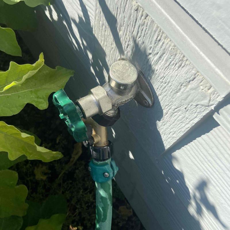 Hose faucet with green handle on house exterior wall