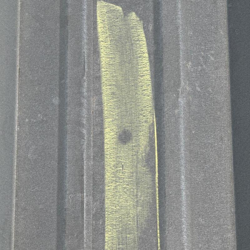 Metal roof panel with hail damage marked in yellow