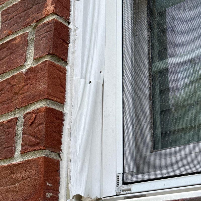 Window frame trim with dents and damage near brick wall