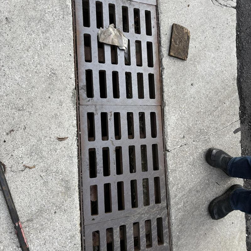 Storm drain grate with debris on concrete sidewalk Storm drain grate with debris on concrete sidewalk