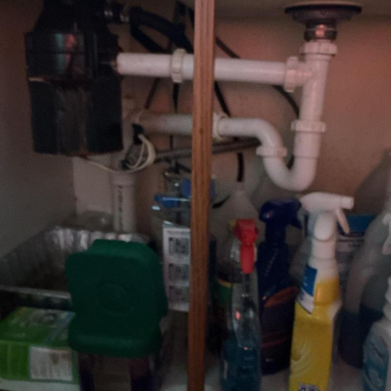 PVC drain pipes and trap under a kitchen sink with cleaning supplies PVC drain pipes and trap under a kitchen sink with cleaning supplies