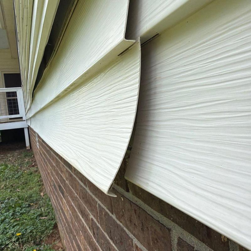 Vinyl siding panels warped and detached from brick wall