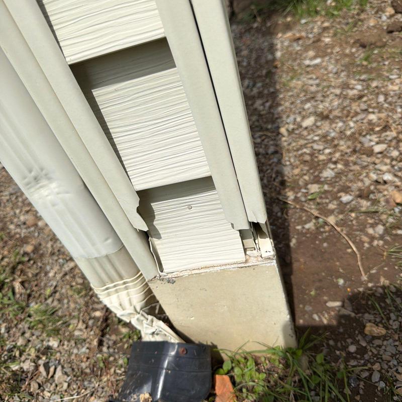 Vinyl siding corner damage near downspout base