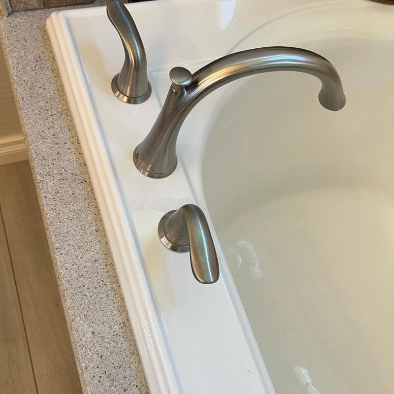 Bathtub faucet and handles installed on white tub edge