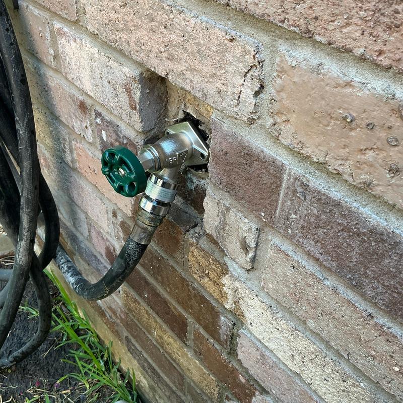 Frost proof hose bib with attached garden hose on brick wall