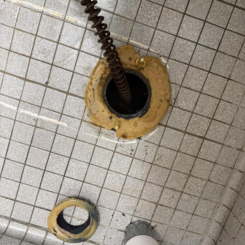 Main floor drain pipe with plumbing snake in tiled bathroom Main floor drain pipe with plumbing snake in tiled bathroom