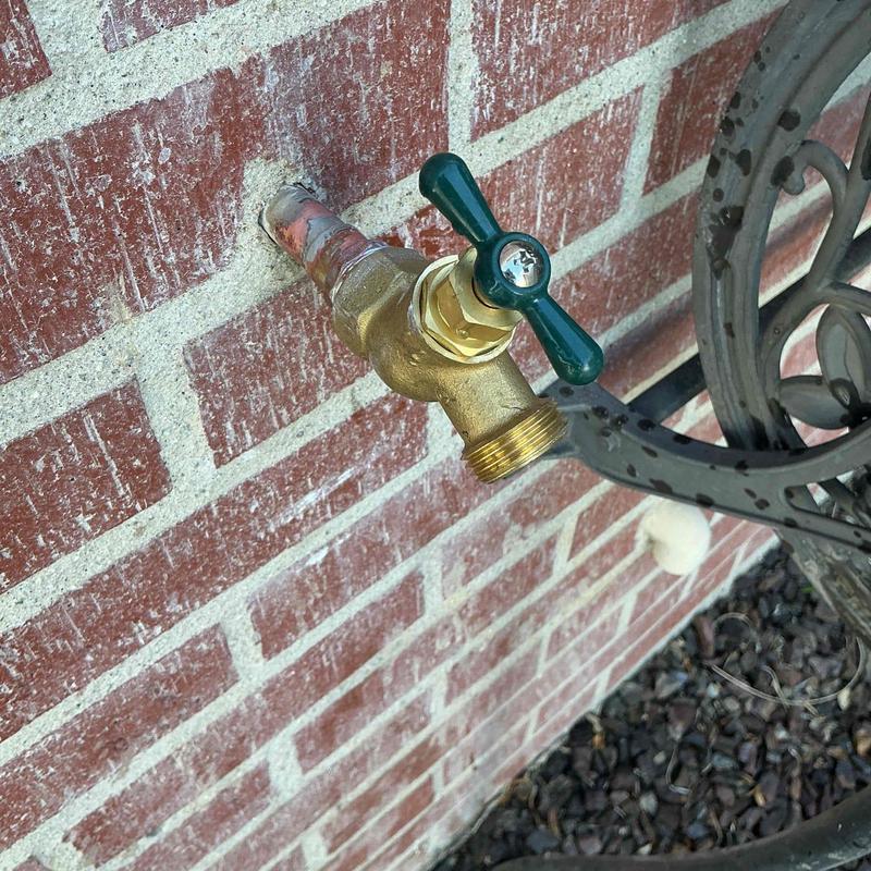Outdoor brass hose bib with green handle installed on brick wall
