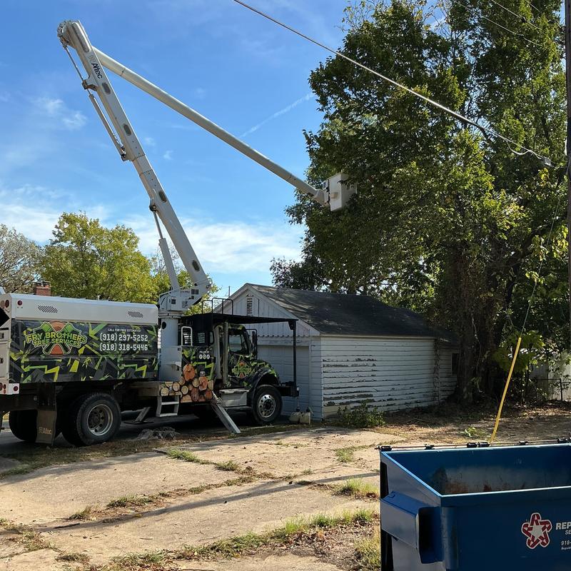 Bucket truck trimming trees near power lines and garage