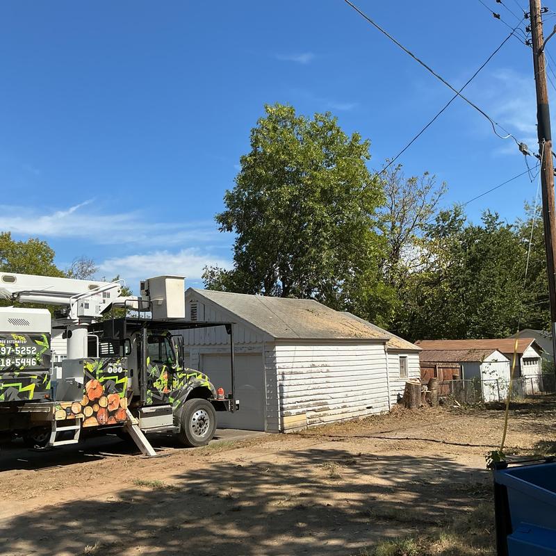 Bucket truck beside garage trimming trees near power lines