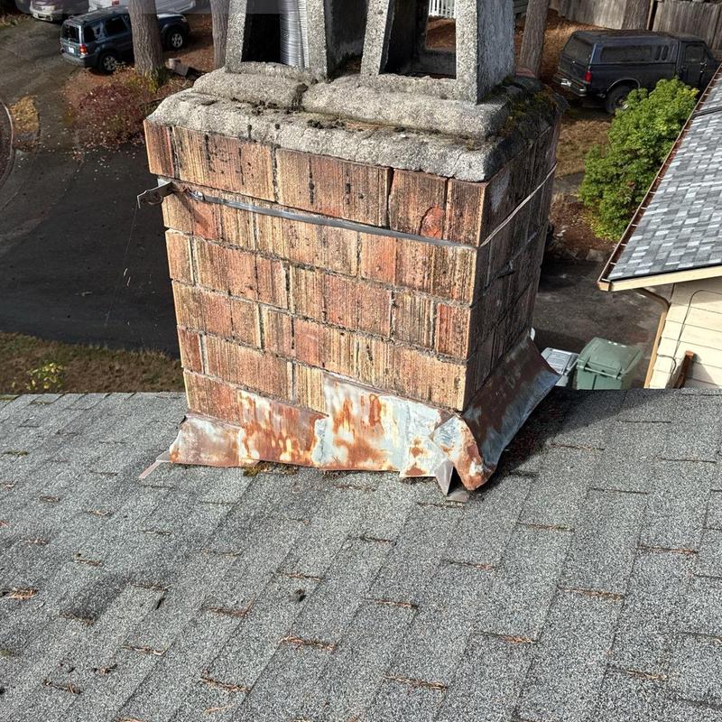 Brick chimney with rusted metal flashing on shingle roof