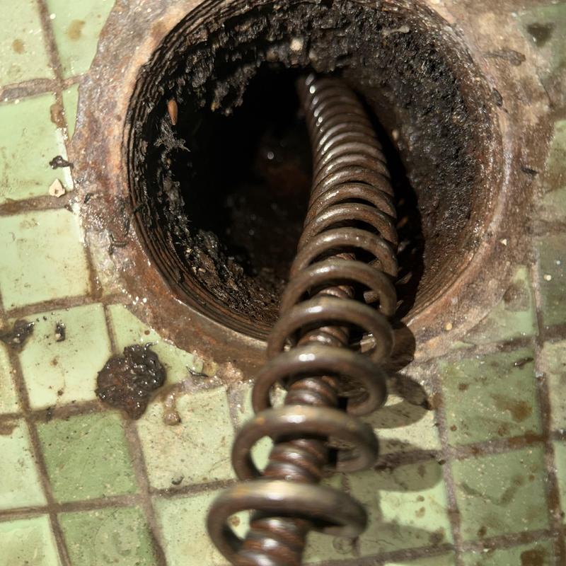 Main line drain cleaning coil inside pipe on tiled floor Main line drain cleaning coil inside pipe on tiled floor