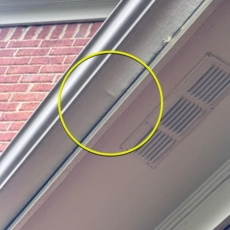 Rain gutter with dented metal section near soffit ventilation