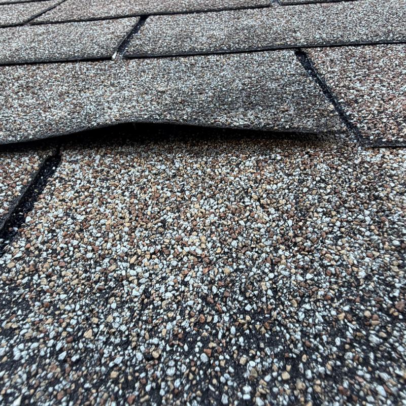 Worn three-tab asphalt shingles lifting on roof surface Worn three-tab asphalt shingles lifting on roof surface